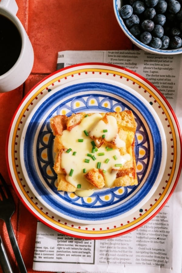 A slice of Eggs Benedict Casserole on a plate topped with Hollandaise sauce and chives.