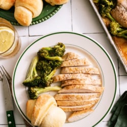 A plate of Sheet Pan Honey Lemon Chicken on a plate with broccoli and a roll.