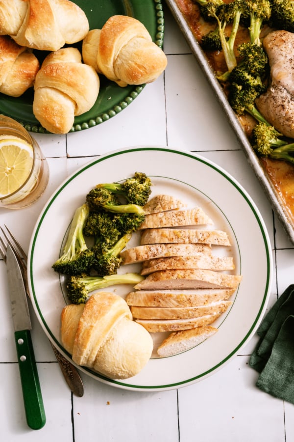 A plate of Sheet Pan Honey Lemon Chicken on a plate with broccoli and a roll.
