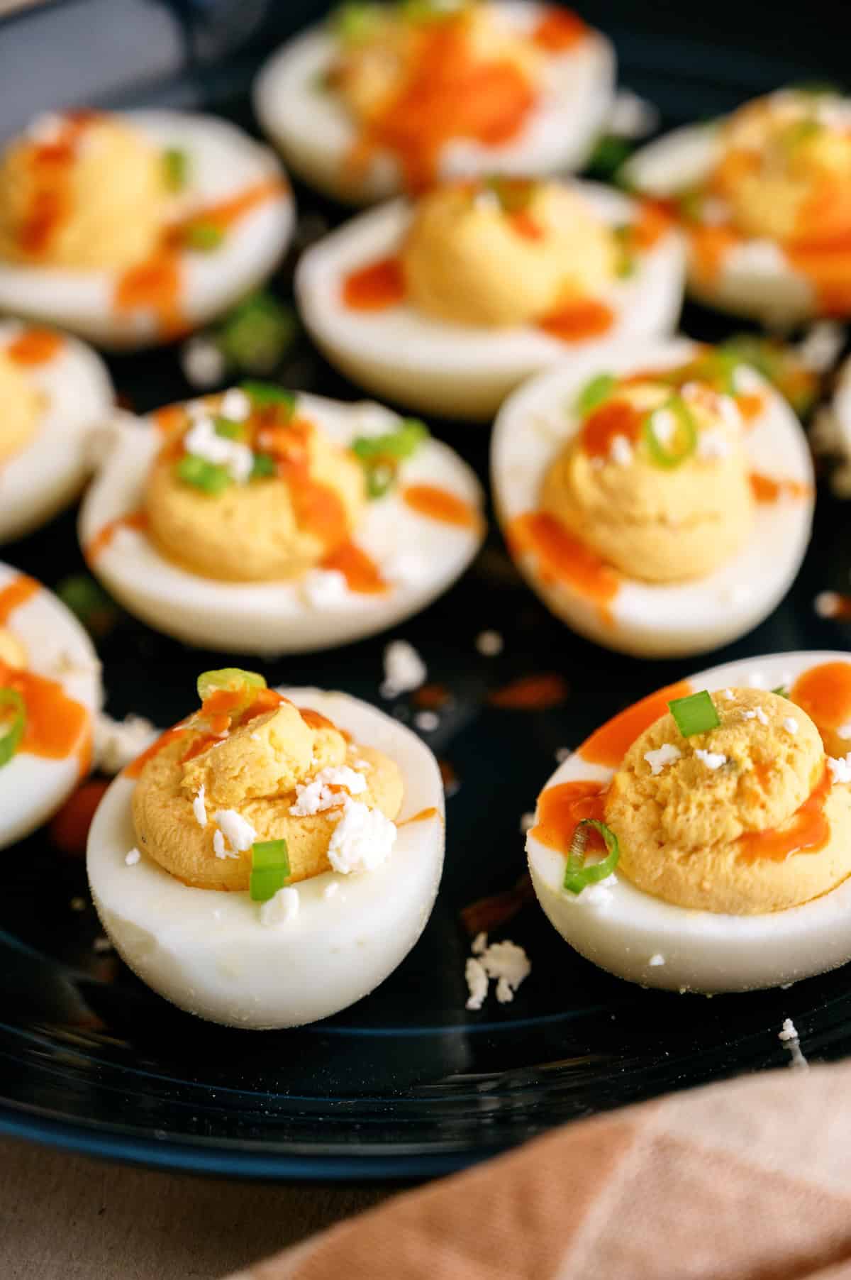 A plate of deviled eggs topped with hot sauce, chopped green onions, and crumbled cheese.
