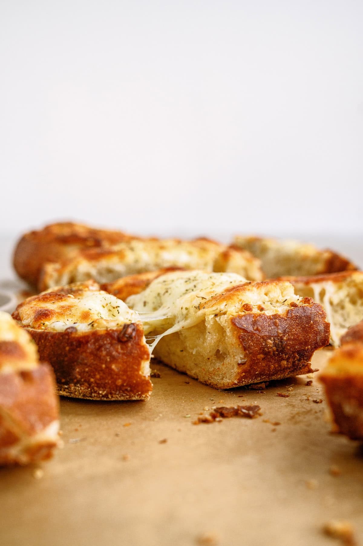 Slices of golden-brown garlic bread with melted cheese, arranged on parchment paper with a white background.
