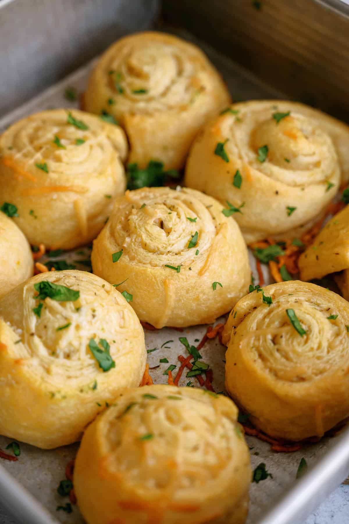 A close-up of baked pastry pinwheels topped with chopped herbs in a metal baking pan.