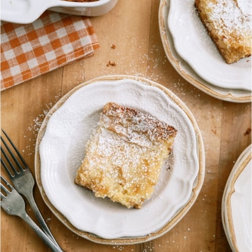 A slice of Gooey Butter Cake on a plate sprinkled with powdered sugar.