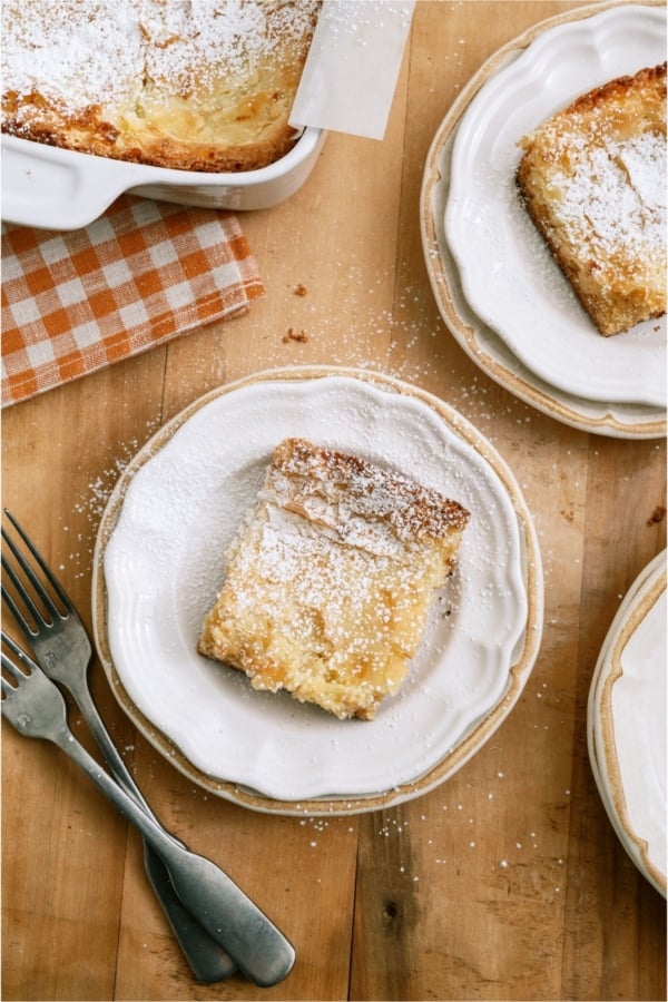 A slice of Gooey Butter Cake on a plate sprinkled with powdered sugar.