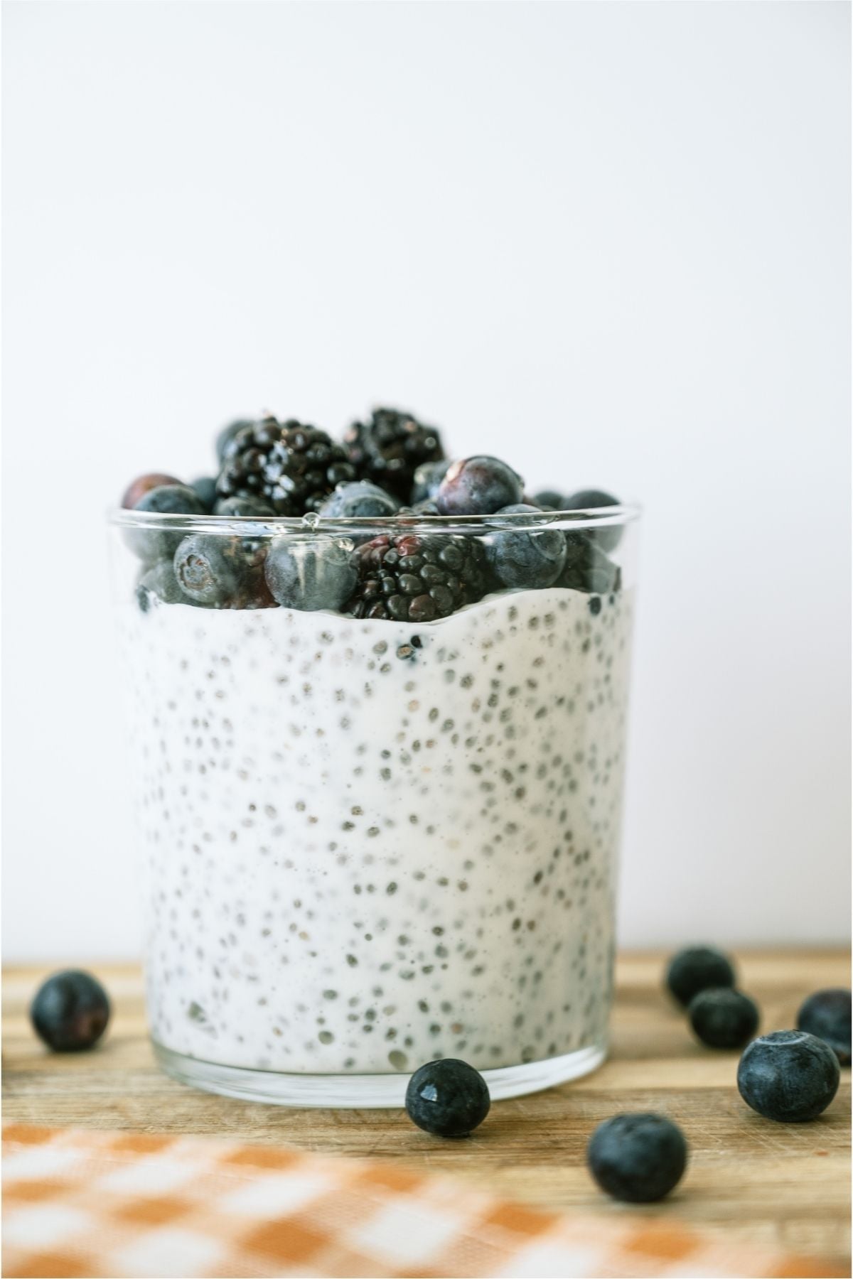 A glass of Overnight Chia Pudding surrounded by fresh blueberries.
