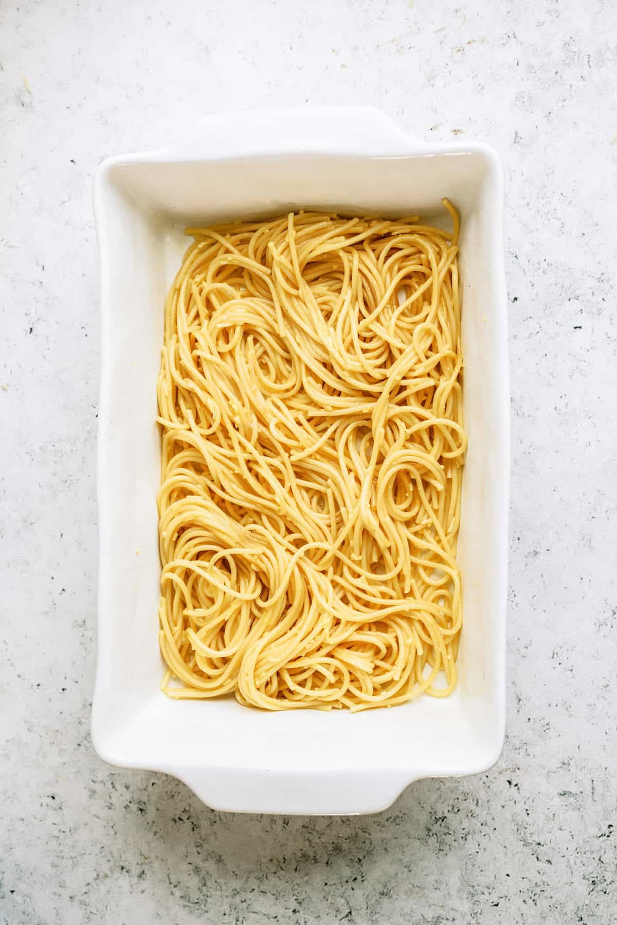 A white rectangular baking dish filled with plain cooked spaghetti noodles on a light, textured surface.