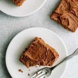 Three square pieces of chocolate-frosted cake are on white plates; one plate has a fork and a partially eaten piece.