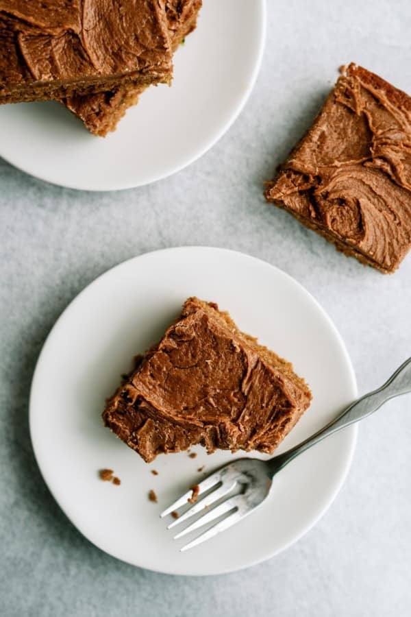 Three square pieces of chocolate-frosted cake are on white plates; one plate has a fork and a partially eaten piece.