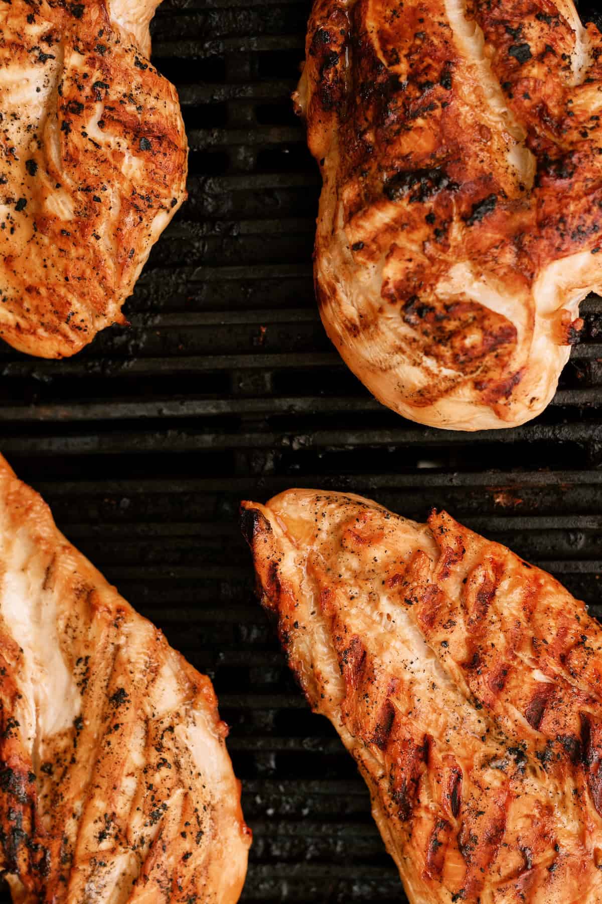 Grilled chicken breasts with char marks cooking on a black grill grate.