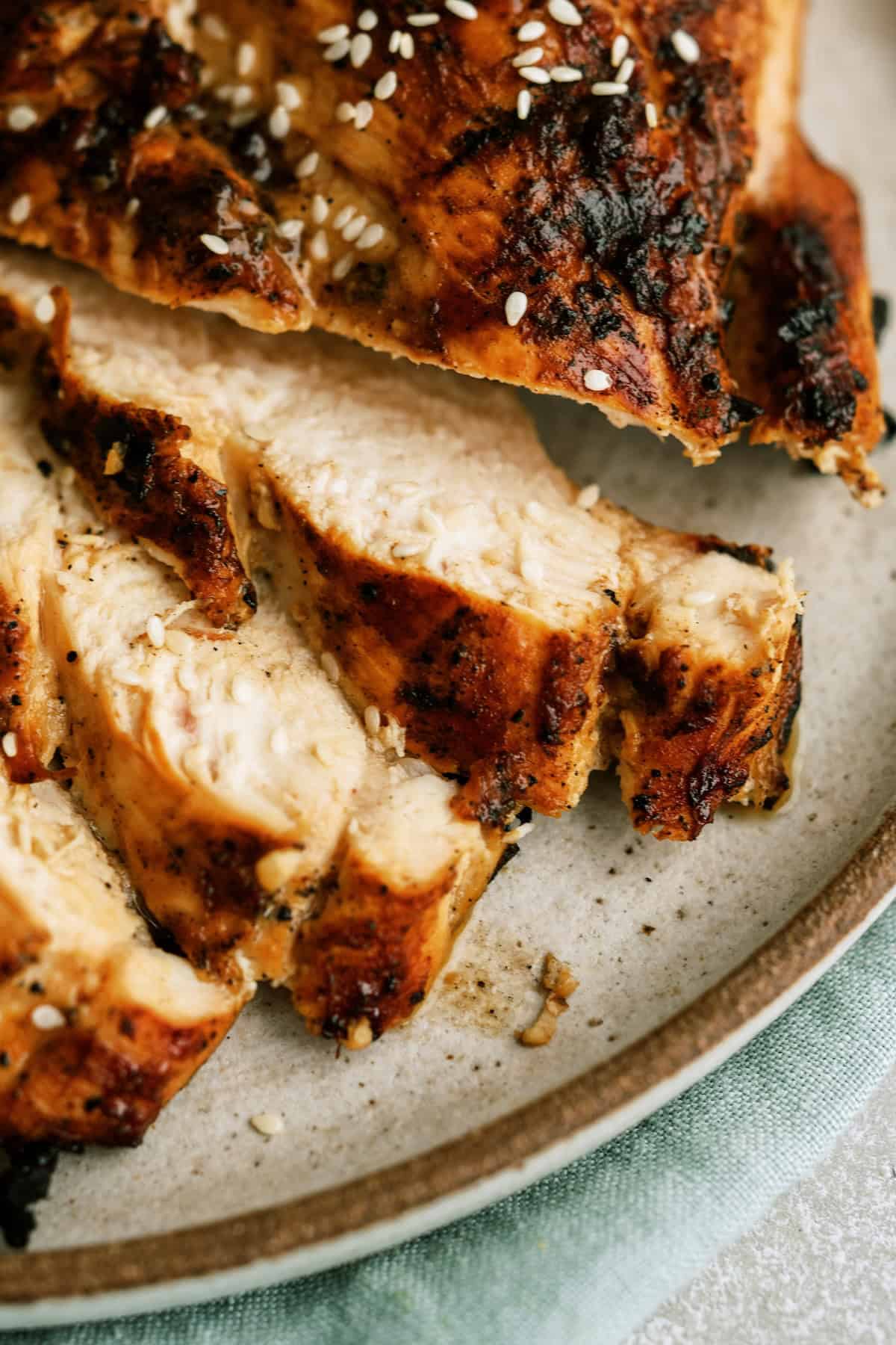 Sliced grilled chicken breast with grill marks and sesame seeds on a plate.