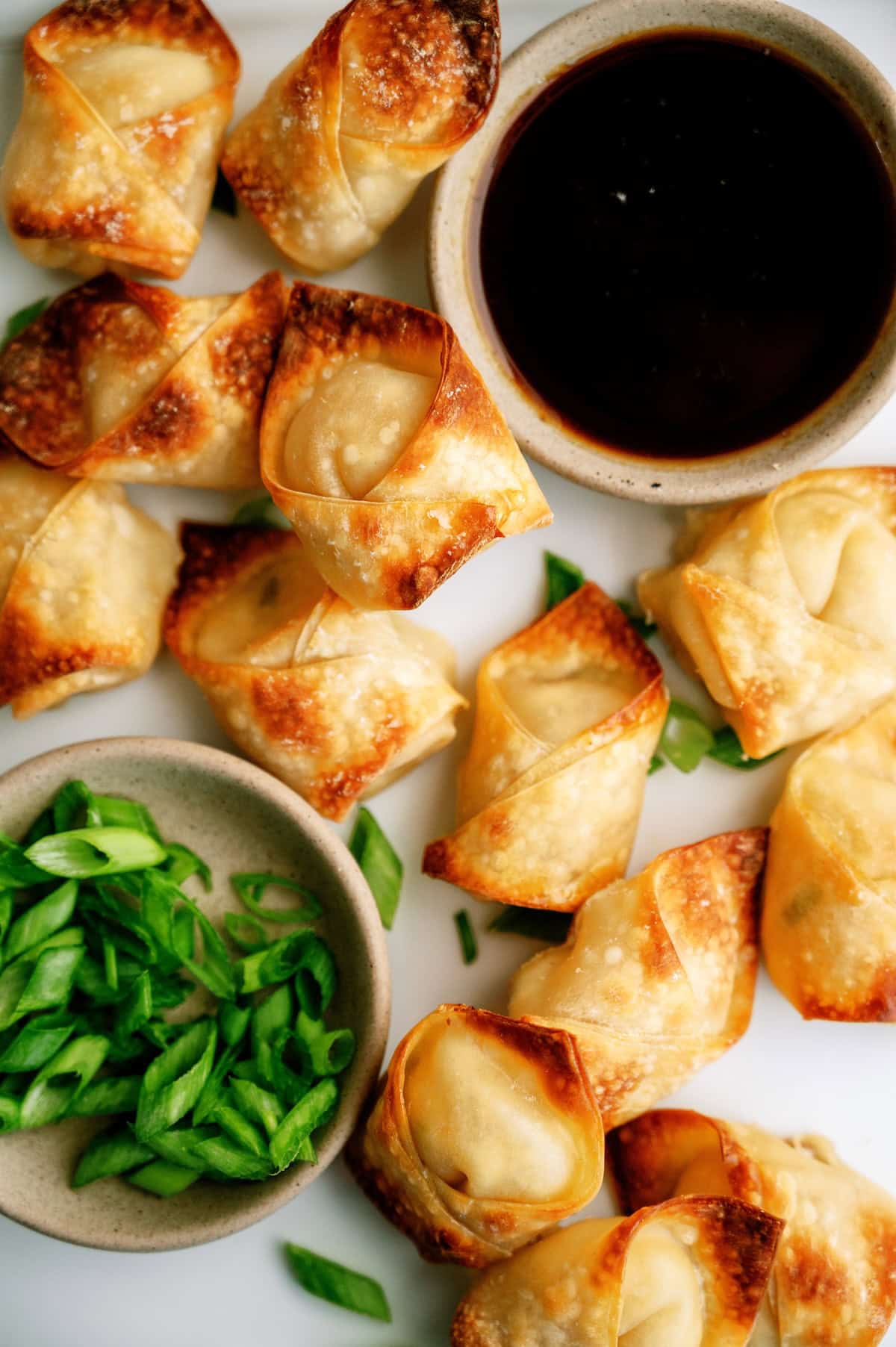 A plate of golden-brown wontons with bowls of soy dipping sauce and sliced green onions on the side.