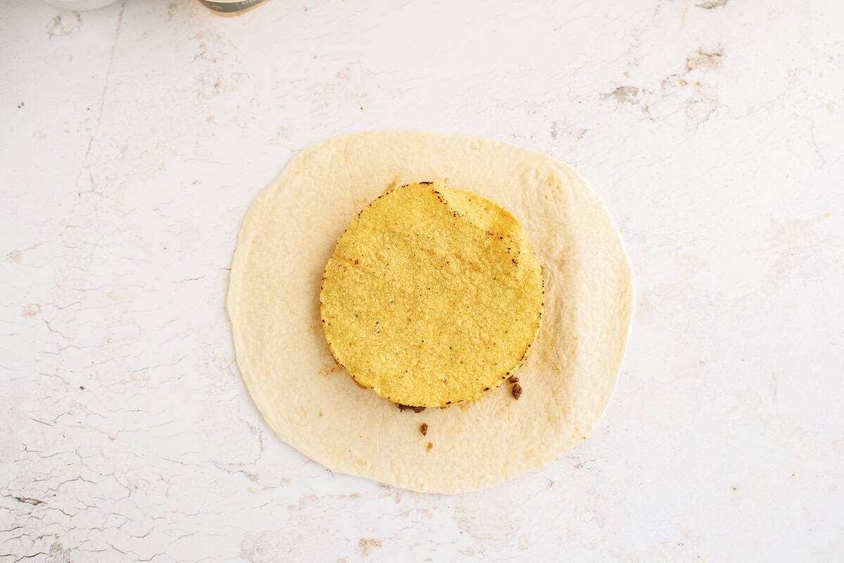 A round, breaded patty placed on an uncooked circular piece of dough on a white, textured surface.