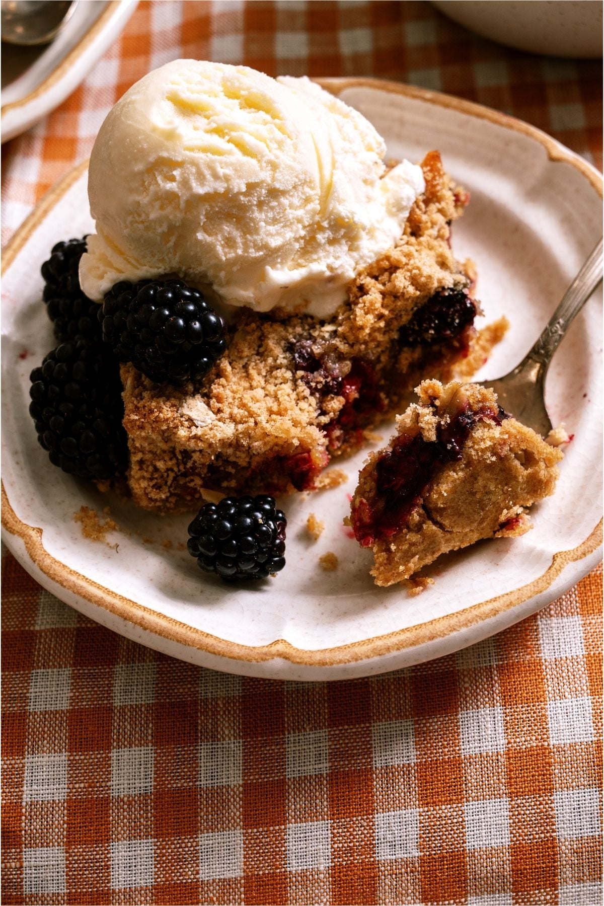 A serving of Blackberry Crumble on a plate topped with a scoop of ice cream.