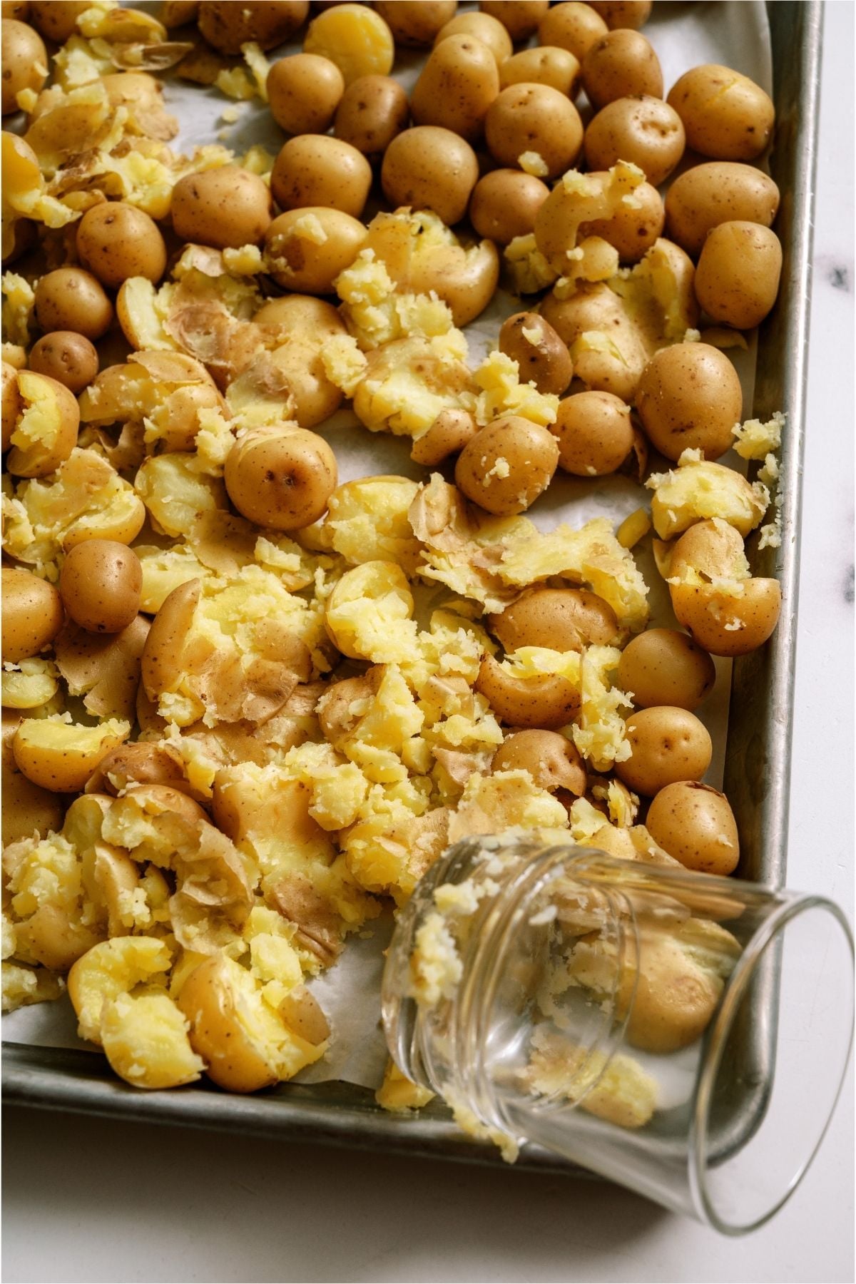 Baby potatoes on a sheet pan getting smashed with a glass.