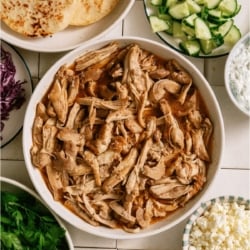 A bowl of Slow Cooker Chicken Shawarma surrounded by pita bread and toppings in bowls.