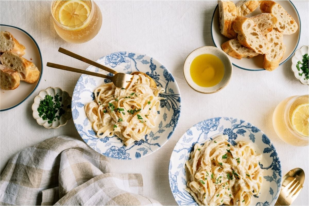 Top view of two bowls of No Fail Fettuccine Alfredo with a plate of bread and drinks.