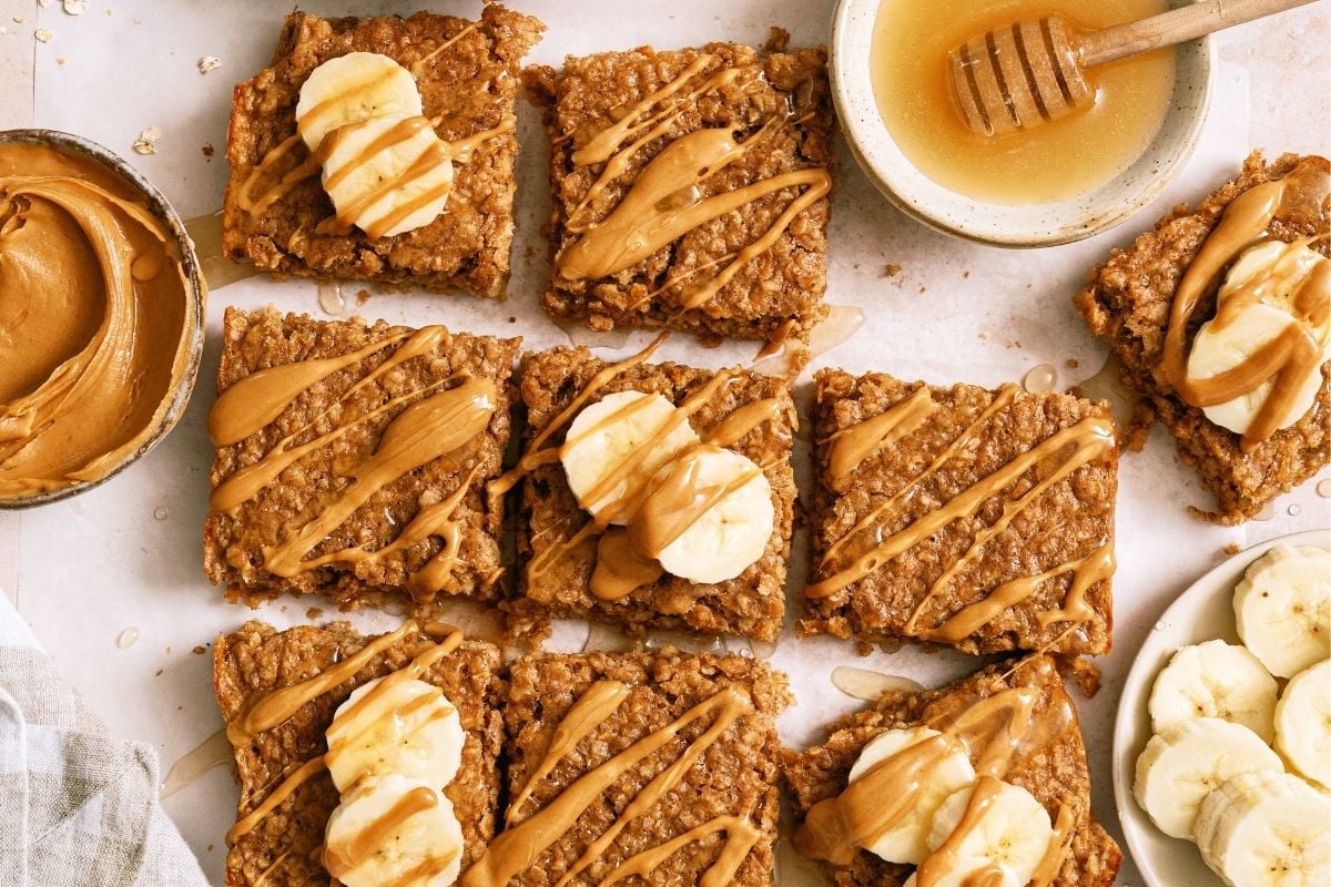 9 Peanut Butter Banana Oatmeal Squares surrounded by bowls of peanut butter, honey and oats.