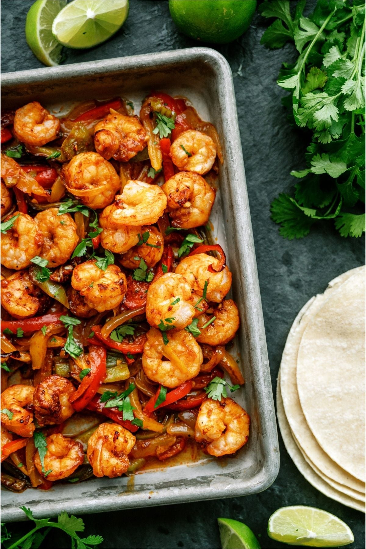 Sheet Pan Shrimp Fajitas on a sheet pan with tortillas and garnishes on the side.