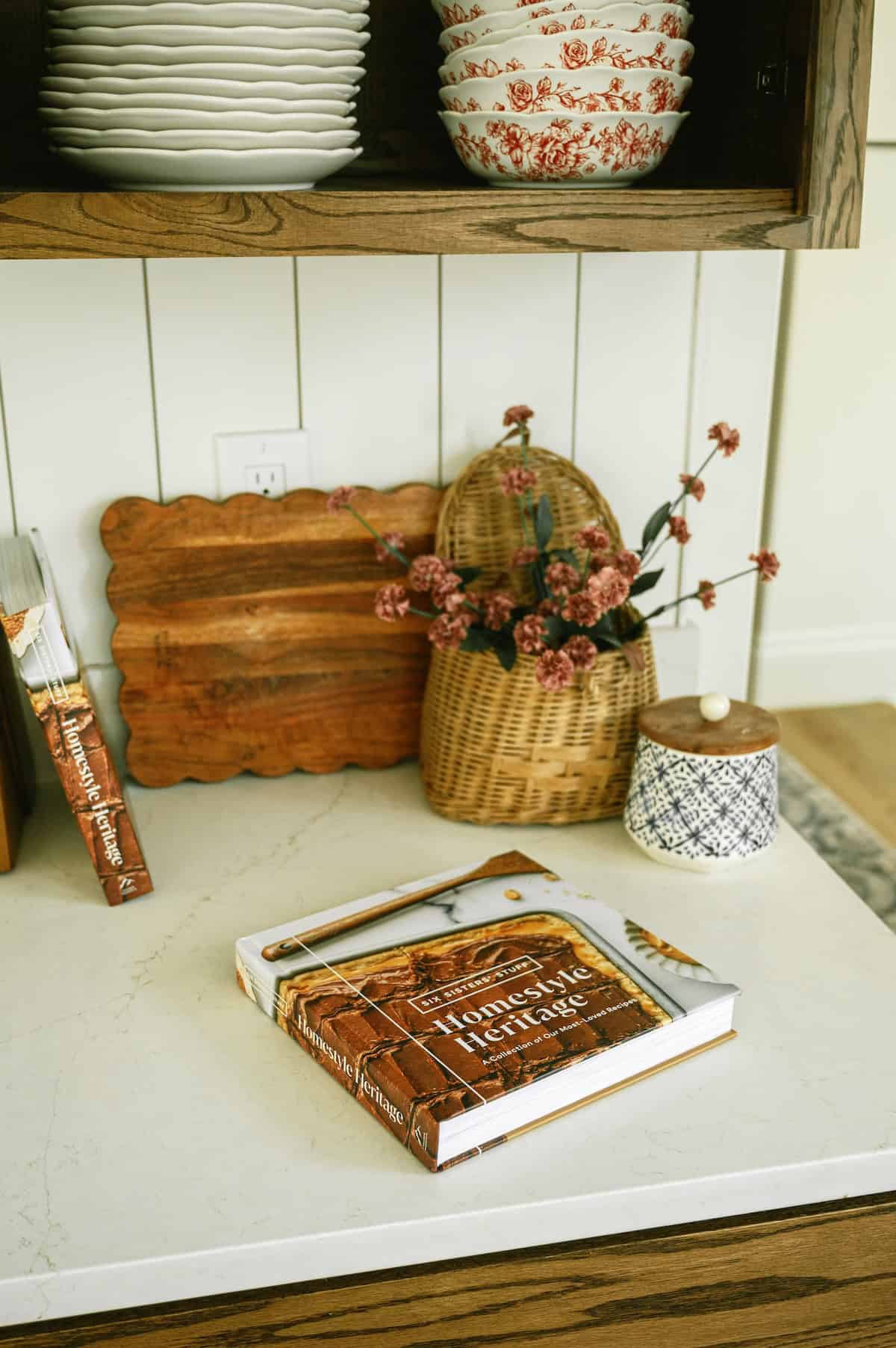 Decorative kitchen shelf with vintage bowls, baskets, and a cookbook.