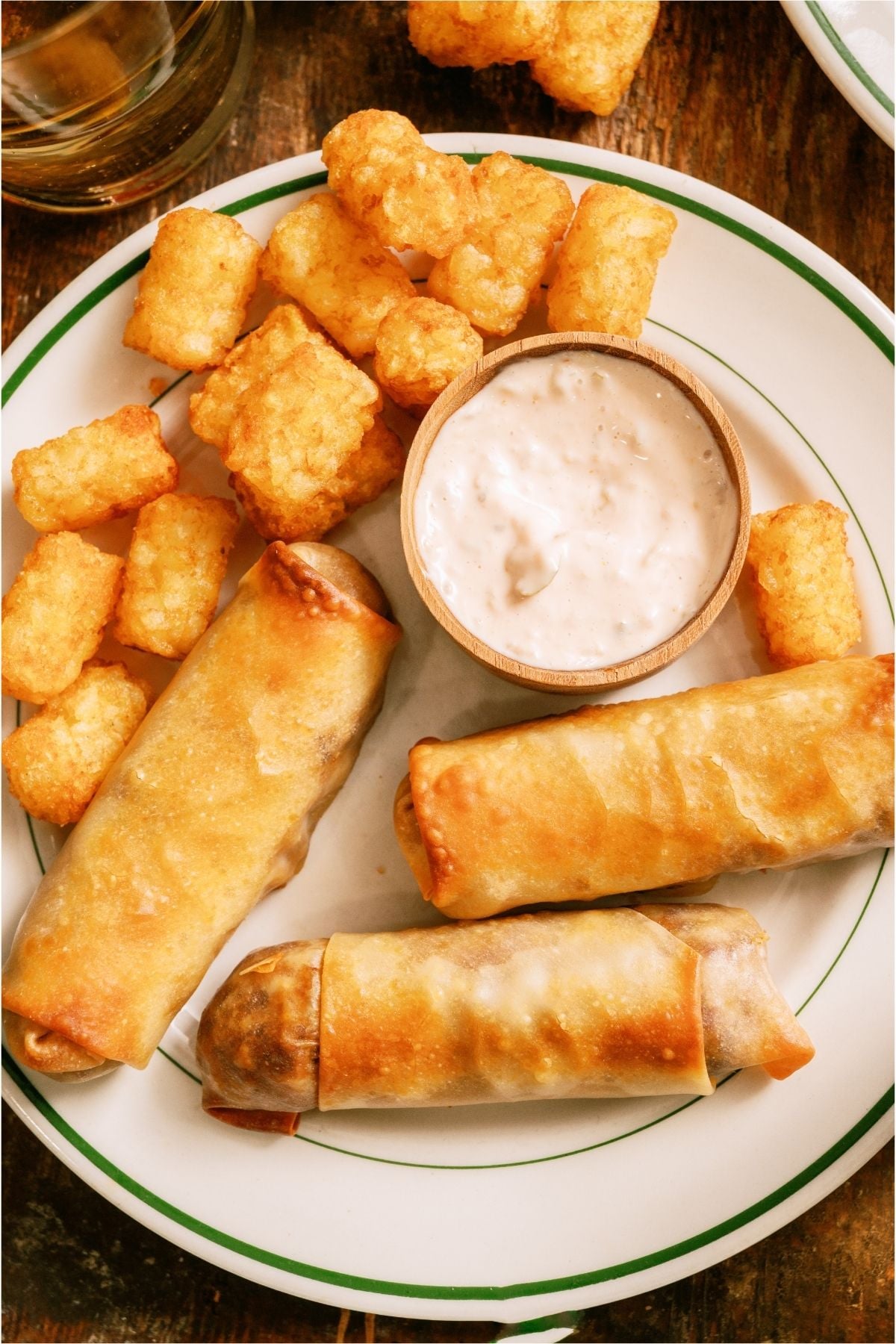 Top view of egg rolls and tater tots on a plate with dipping sauce.