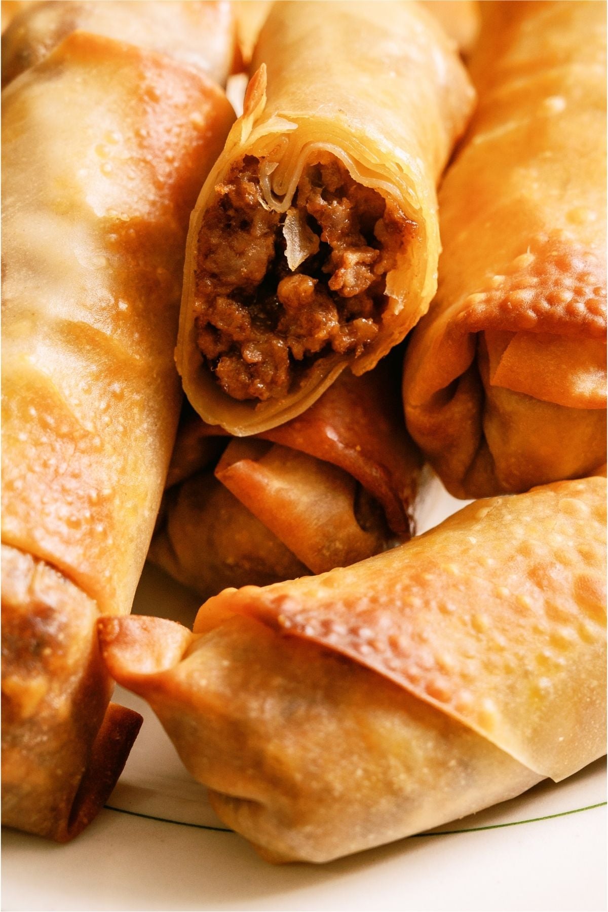 A plate of Cheeseburger Egg Rolls with one cut in half to show the inside.