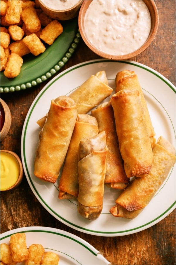 Top view of a plate of Cheeseburger Egg Rolls with dipping sauce and tater tots on the side.