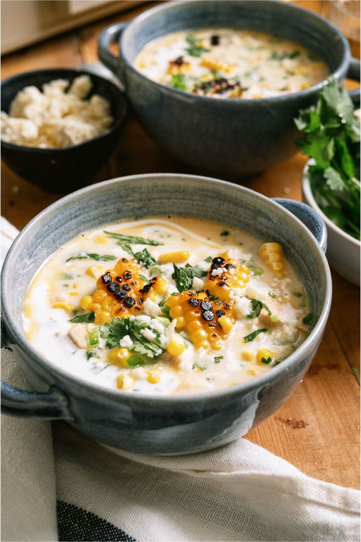 Two bowls of Slow Cooker Street Corn Soup next to a small bowl of cheese.
