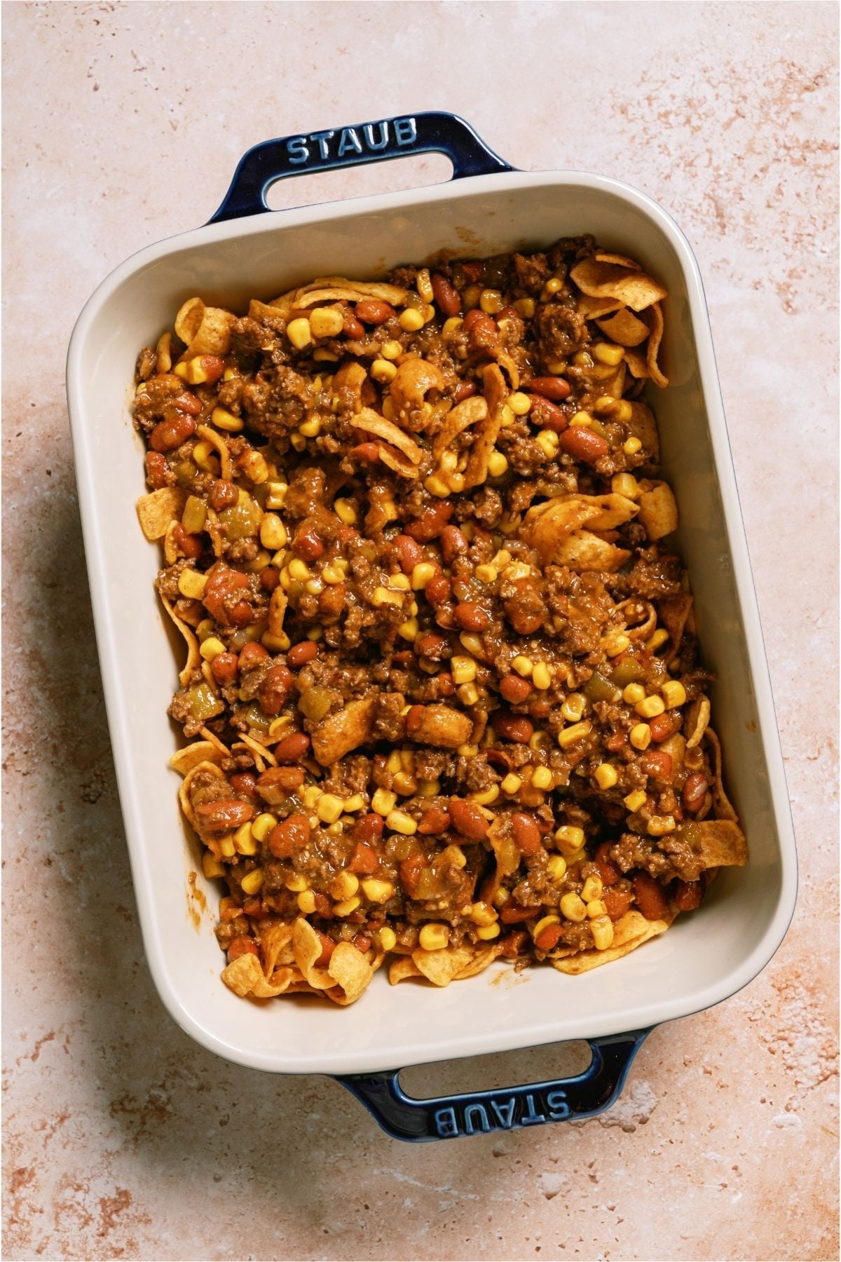 Ground beef on top of frito chips in a casserole dish.
