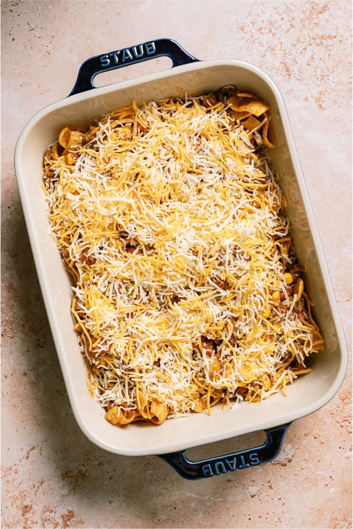Shredded cheese on top of group beef and frito chips in a casserole dish.