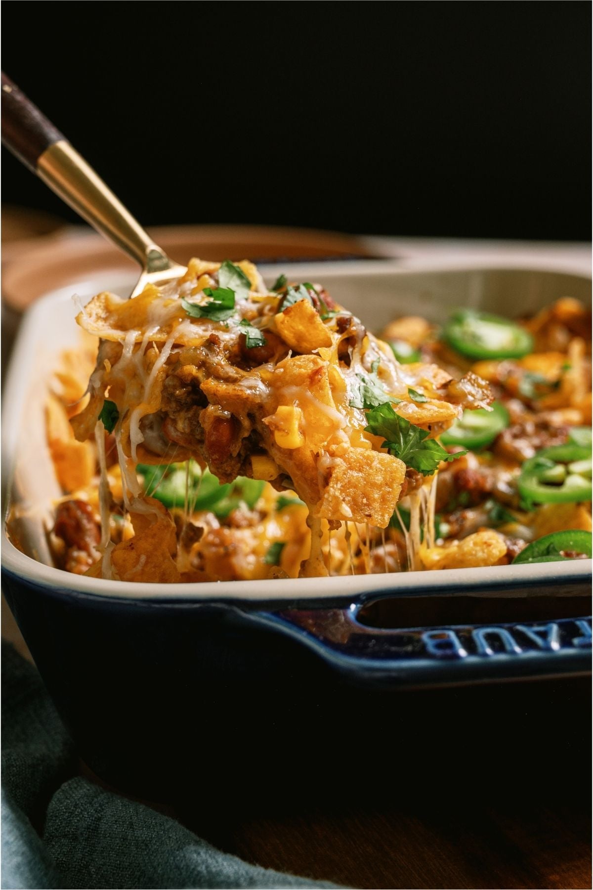 A serving spoon lifting a scoop of Frito Pie out of the casserole dish.