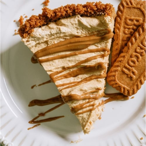 Top view of a slice of No Bake Biscoff Cheesecake on a plate with some biscoff cookies.