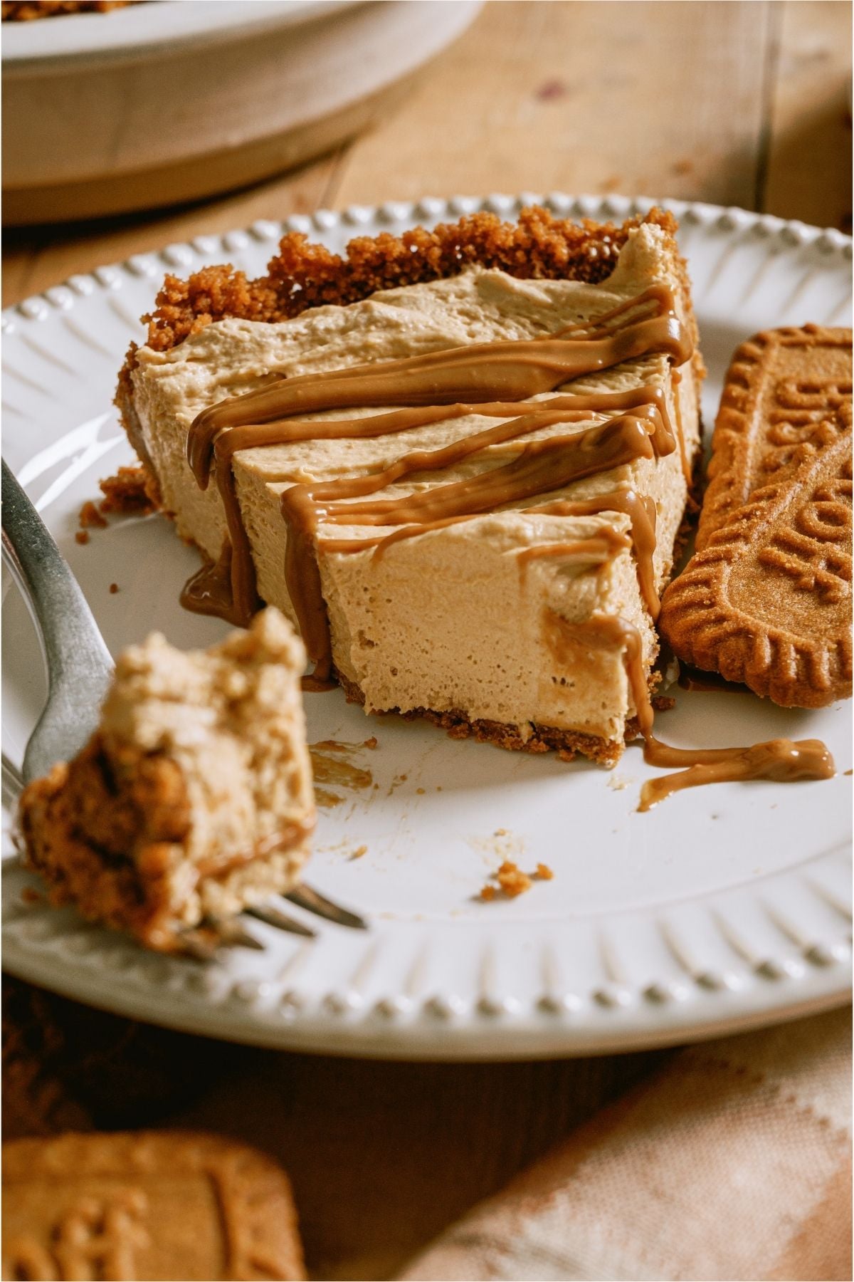 A slice of No Bake Biscoff Cheesecake on a plate with biscoff cookies and a fork taking a bite.